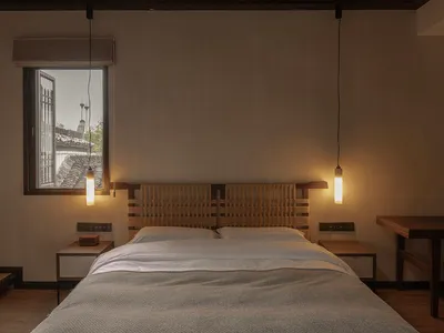A modern minimalist bedroom with a wooden bed frame, grey bedding, and industrial-style pendant lights hanging from the ceili