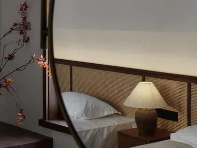 A minimalist bedroom featuring a white bed with a cane-weave headboard and a warm, ambient light.