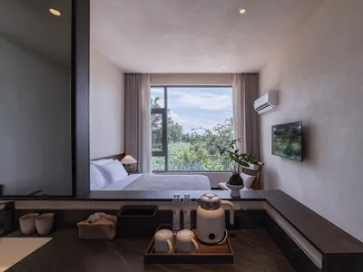 A minimalist bedroom with wooden furniture, stone accents, and glass window overlooking a natural landscape.