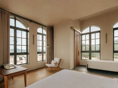 Modern minimalist bedroom with a white bed, wooden floor, and large windows.