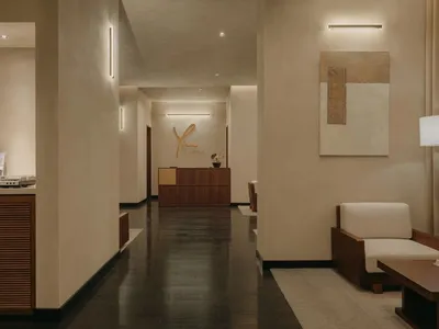 Modern, minimalist hotel reception area with sleek, dark wood flooring, beige seating, and a sleek reception desk with the ho