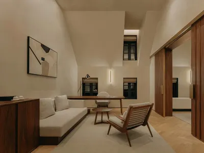 A minimalist living room with a white sofa, wooden armchair, and wooden desk.