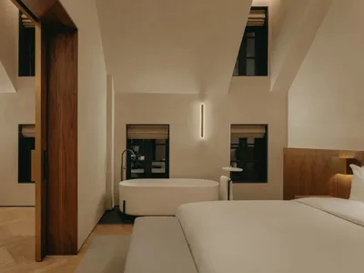 Modern minimalist bedroom featuring a white bed, white bathtub, and beige walls with plaster finish.