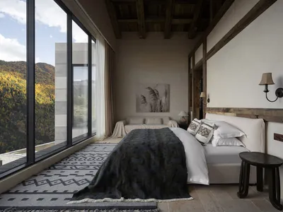 A modern minimalist bedroom with white-on-white bedding, a wooden headboard, and a large window overlooking the mountains.