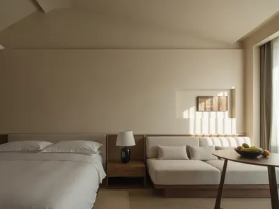 A serene minimalist bedroom with a bed, couch, and a fruit bowl on a table.