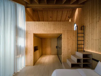 A minimalist bedroom featuring wooden walls and a white bed, with a ladder leading up to an upper floor.