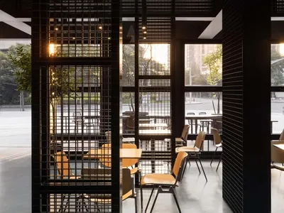 Industrial-style restaurant interior with black lattice walls, concrete flooring, and chairs with wooden seats.