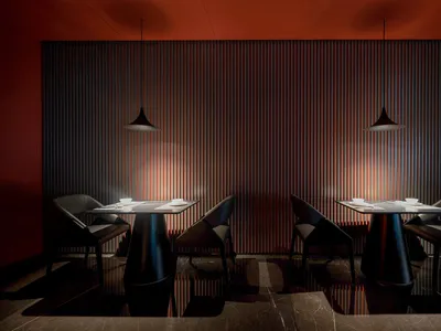 Two modern restaurant tables with metal bases and wooden tops, set against a striped metal backdrop and illuminated by pendan