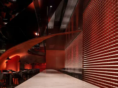 A modern restaurant interior with a red metallic tile wall and sleek bar counter.