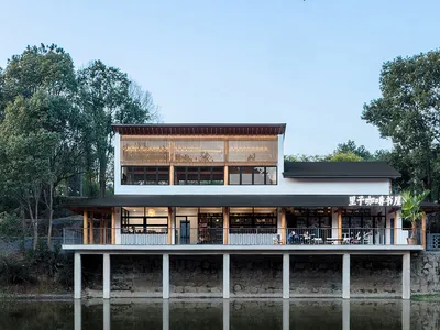 Modern restaurant building with wooden accents and concrete columns surrounded by calm water