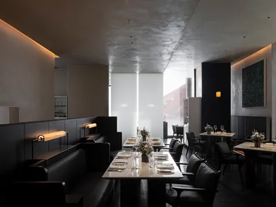 A modern restaurant with concrete walls and benches, featuring sleek furniture and minimalist decor.