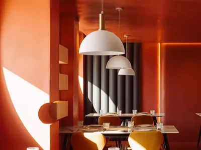 A modern restaurant interior featuring white pendant lights hanging from an orange ceiling.