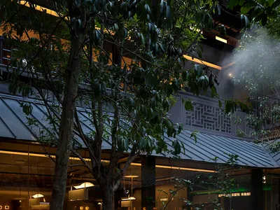 Outdoor view of an industrial-themed restaurant with metallic accents, glass walls, and a concrete structure.