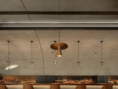 A modern bar interior featuring a concrete wall, wooden accents, and minimalist lighting.