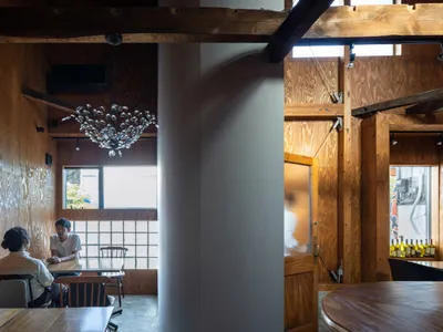 A modern restaurant interior with wooden walls and seating areas, featuring a chandelier and a glass partition.