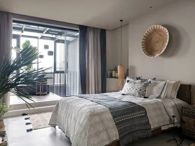 A boho-style bedroom featuring a bed with a woven headboard and decorative textiles, alongside ceramic and woven elements.