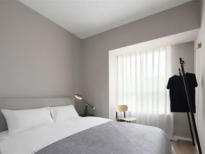 Minimalist bedroom featuring a bed with neutral-toned bedding, a table lamp, and a window with sheer curtains.