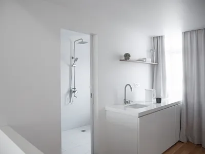 A minimalist kitchen with a white countertop, cabinets, and floor, featuring a window with sheer curtains.