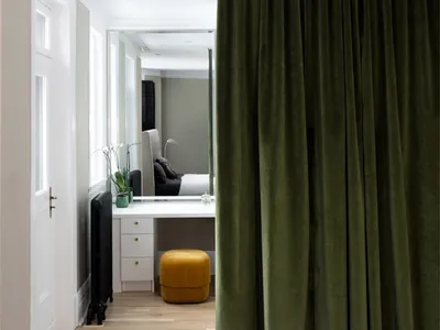 Modern bedroom with green velvet curtain, white walls, hardwood floor, and black radiator.