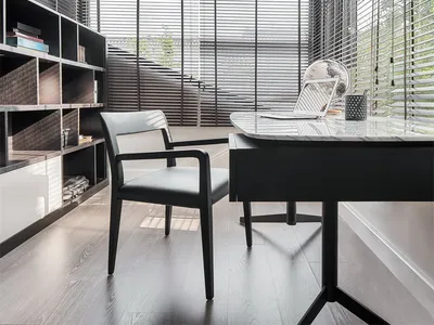 Modern home office featuring a sleek black desk and comfortable chair, surrounded by large windows with natural light streami