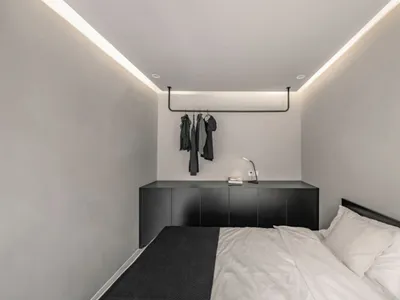 Minimalist bedroom with a white bed and black furniture, featuring textured white walls and a black rug.
