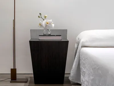 A minimalist bedroom with a wooden side table featuring a vase of white flowers and a book.