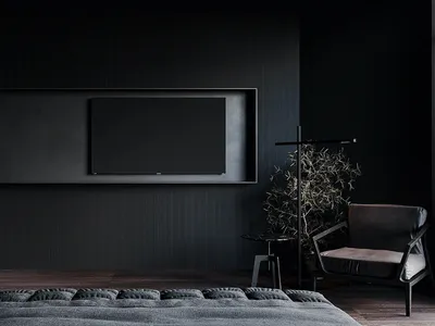 A minimalist bedroom with a dark color palette, featuring a bed with textured bedding, a wall-mounted flat-screen TV, and a s