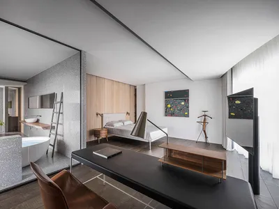 A modern minimalist bedroom featuring a clear glass wall, a wooden headboard, and a large desk.