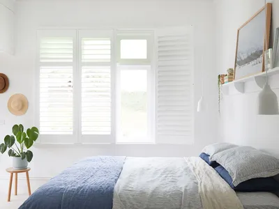 Bedroom with white shutters, blue and white bedding, and a potted plant.