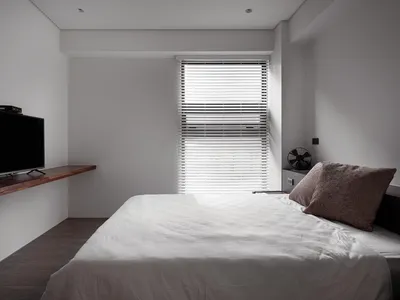 A minimalist bedroom featuring wooden furniture and a bed with a white sheet and a brown pillow.