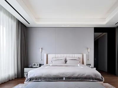 A minimalist bedroom featuring a bed with a textured gray headboard against a textured light gray wall, flanked by sconces an