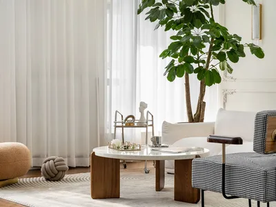 A minimalist living room with white furniture, green plants, and a large window.