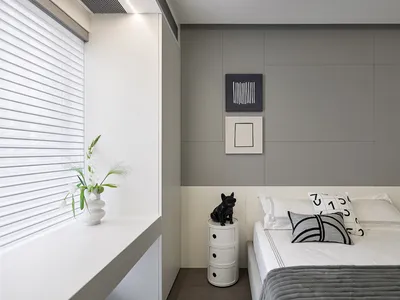 A minimalist bedroom with a grey and taupe color scheme, featuring a bed with white sheets and black and white pillows, a whi