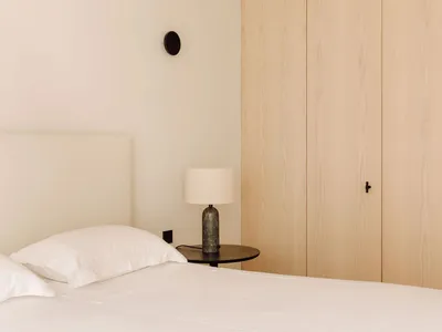 Minimalist bedroom featuring wooden cabinets and a bed with white linens.