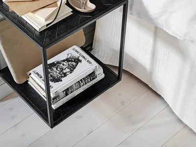 A minimalist bedroom featuring a black side table with a stack of books and a decorative vase.