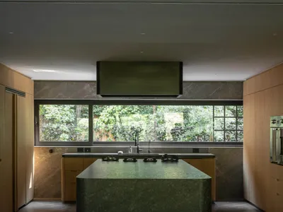 Modern kitchen with a marble island and large windows overlooking greenery.