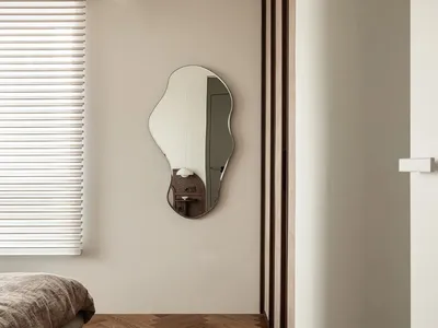 A minimalist bedroom featuring a bed with a wooden frame and a unique shaped mirror hanging on the wall.