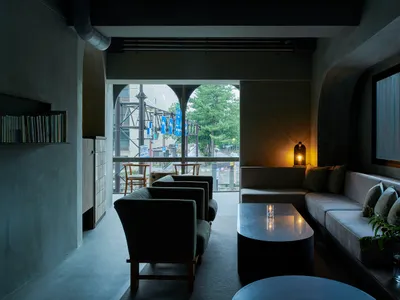 A minimalist industrial living room with concrete walls, large windows, and a modern sofa.