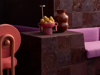 A modern living area with a purple couch, red chair, vases, and apples, creating a cozy and inviting atmosphere with bold colors and simple decorations