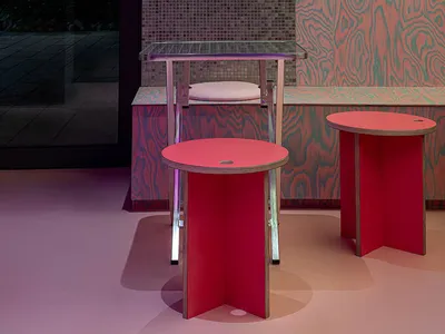 A cozy dining area with a pink table surrounded by metal chairs, natural light from a window, and a warm atmosphere