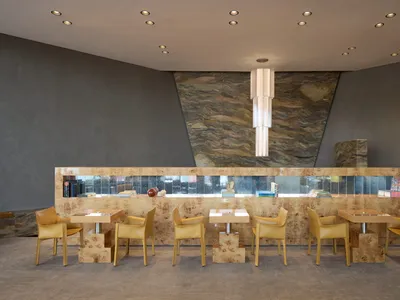 A modern restaurant with a large dining area featuring multiple tables and chairs, stone and wood walls, and warm lighting