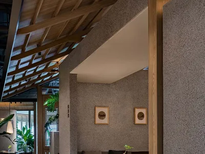 A well-lit living space with a dining table, chairs, potted plants, and a vase, set against a wooden ceiling