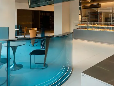 Modern restaurant interior with glass partition separating dining and kitchen areas, featuring tables, chairs, and a kitchen visible through the glass wall