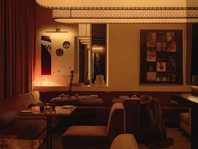 Comfortable living space with two couches, chairs, a dining table, and decorative elements like potted plants, vases, books, and cups, set against a warm brown-colored wall backdrop