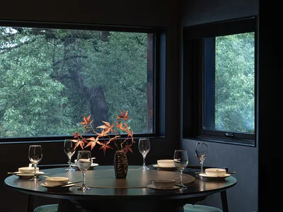 A dining area with a round table, chairs, wine glasses, and vases in a darkened room, creating an intimate atmosphere