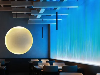 A modern restaurant dining area with a round light fixture hanging from the ceiling, illuminating the space and several chairs around the tables
