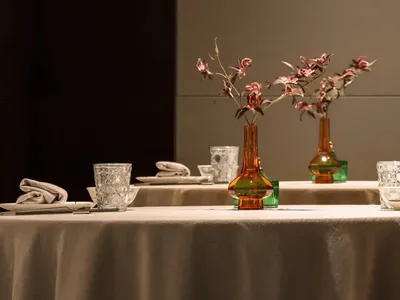 A dining area with a table set for a meal, featuring multiple vases with flowers, utensils, and cups, creating a sophisticated and inviting atmosphere