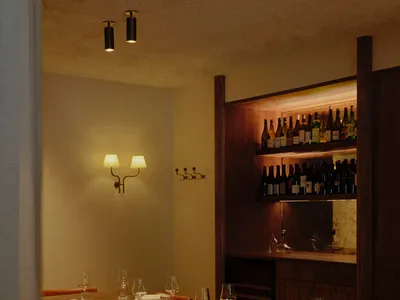 Dimly lit dining space with tables, chairs, and wine glasses, featuring a modern and sophisticated design