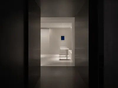 Dark hotel hallway with a black doorway, two tables, and a chair, lacking natural light