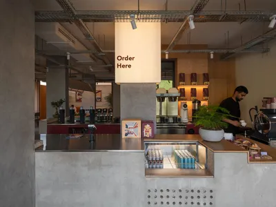 A casual restaurant counter with a cash register, cups, bottles, and potted plants, creating a welcoming atmosphere for customers